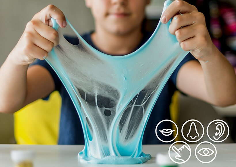 A photo of a boy stretching blue slime between his hands and the table