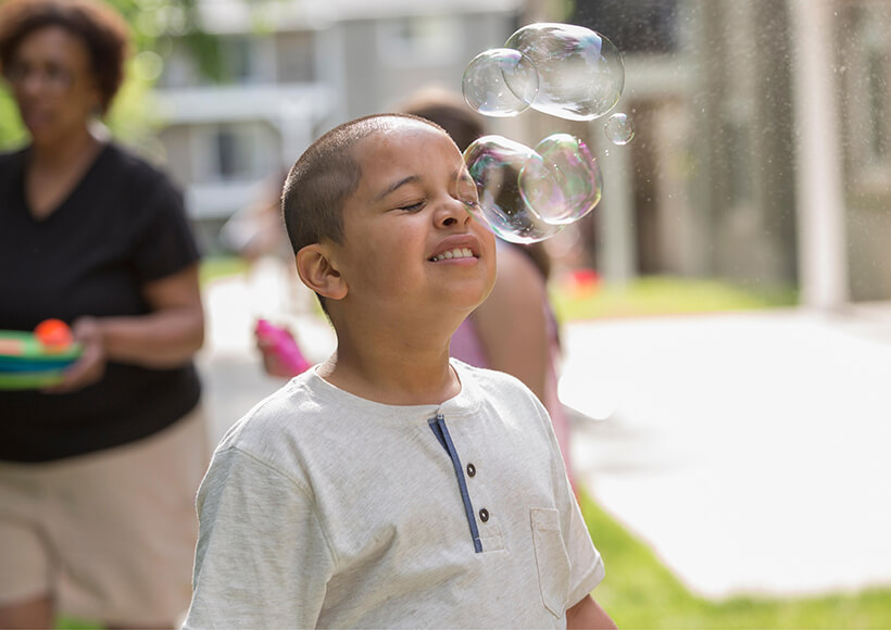 A photo of a boy with his eyes closed about to pop some bubbles with his face