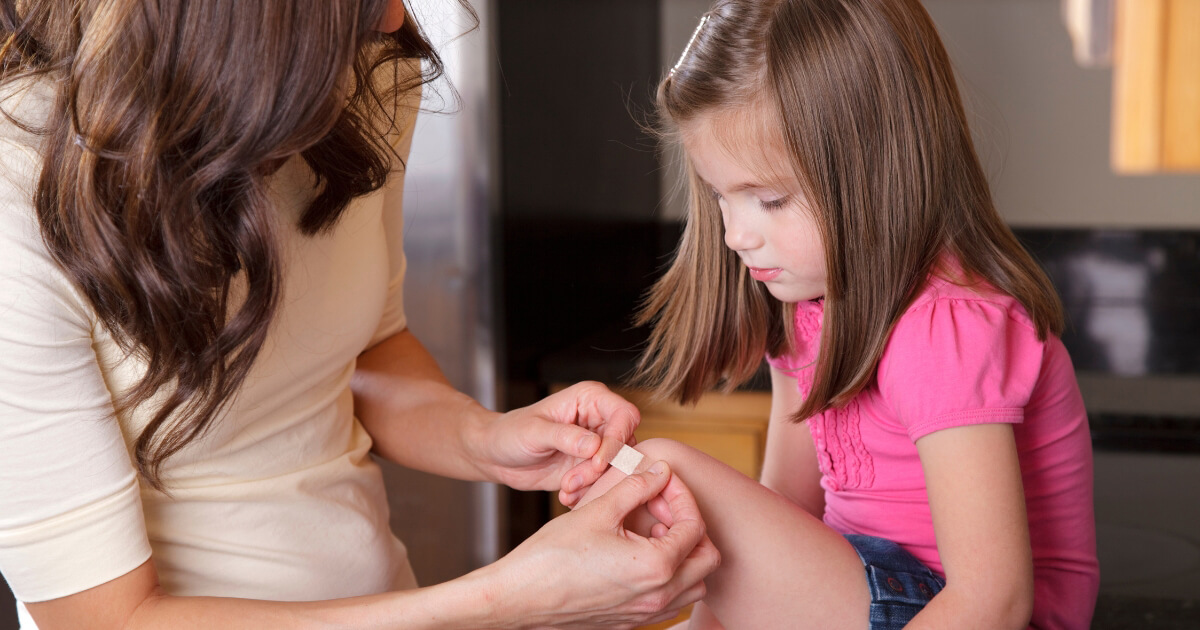 A photo of a young girl having a plaster applied to her knee