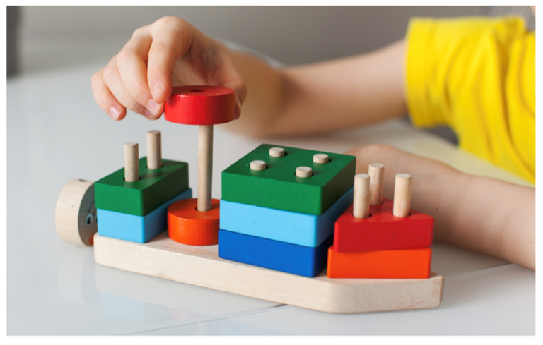 A child's hands placing blocks with holes in onto a board of pegs