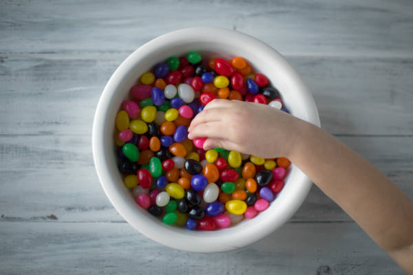 A child's hand reaching toward a bowl of not-nutritious multi-coloured jelly beans