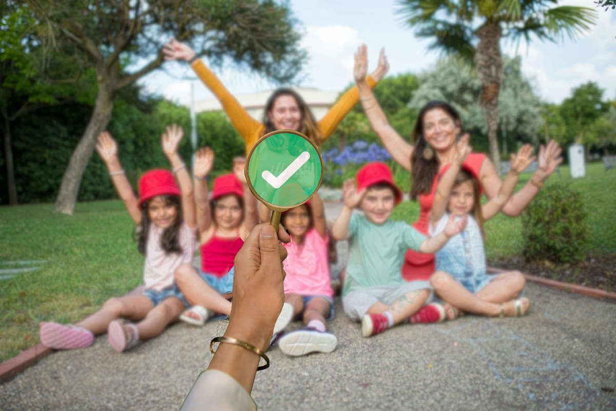 A woman's arm holding up a magnifying glass over a woman with children, shoeing a green circle and white tick