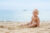 A baby playing in sand on the beach with the sea in the background, likely on a family holiday
