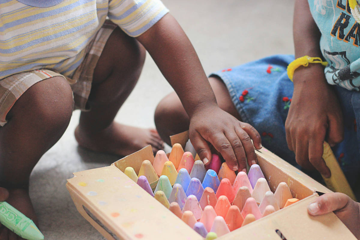 Two children playing with a box of giant chalky crayons