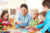 A woman playing with four children at a small table with interlocking building pieces