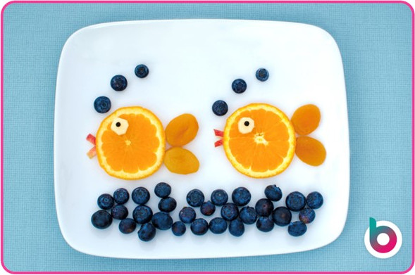 Two fish made from orange slices in a blueberry sea. On a plate