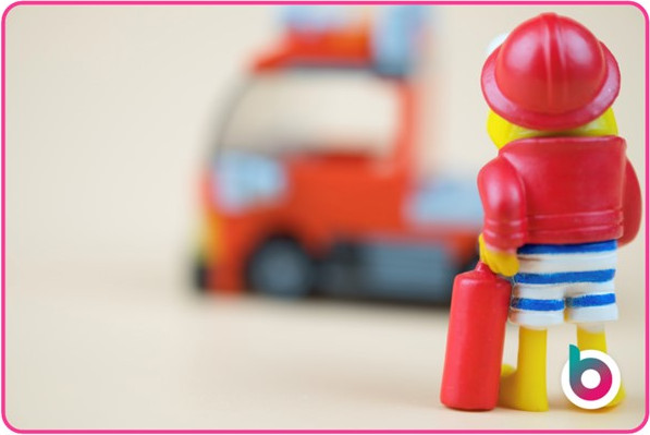 A toy fireman in board shorts looking at a truck in the background