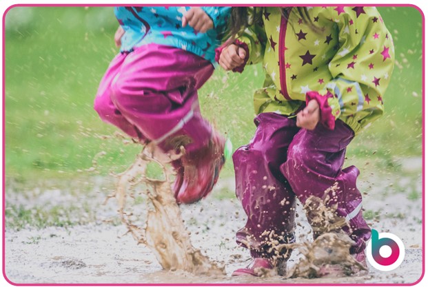 Two children jumping in muddy puddles with wellies on