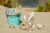 A bucket and toy anchor on a beach filled with under-the-sea- and beach-themed bits